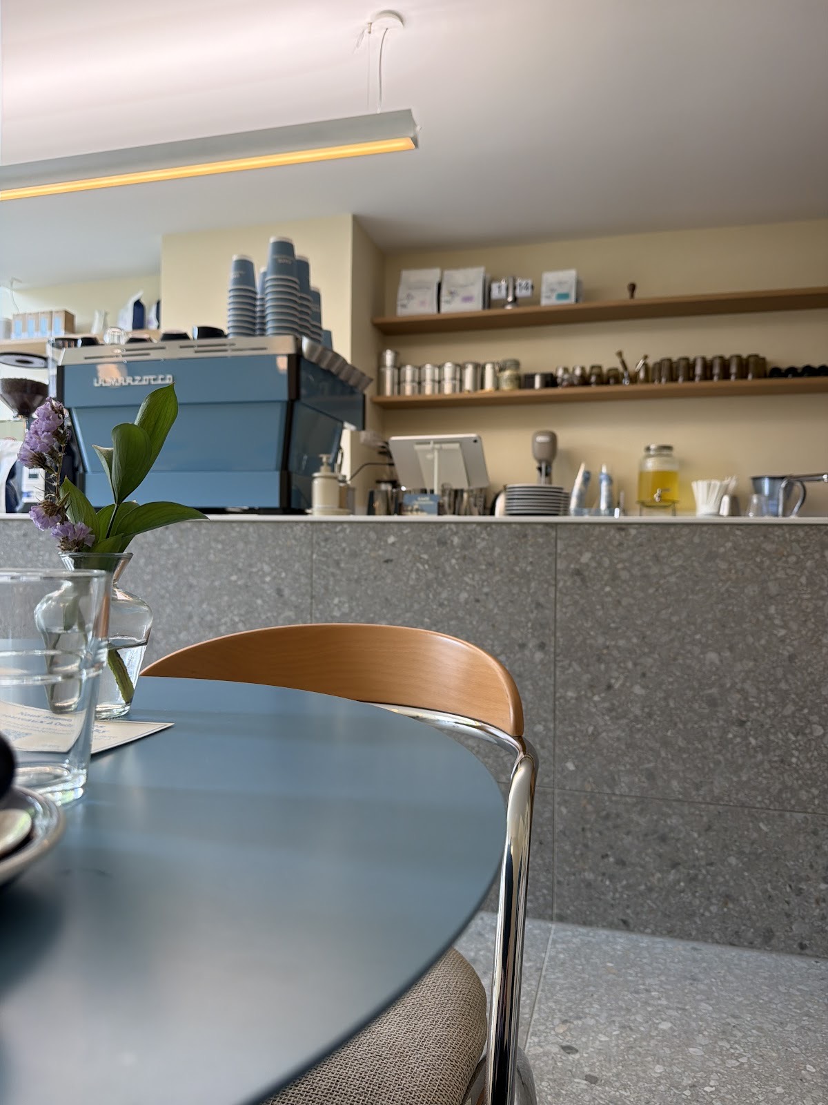 Table bleue, chaise en bouleau et machine La Marzocco au comptoir